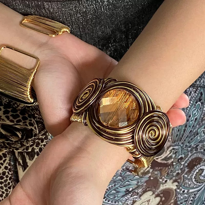 Suka cuff worn on a wrist alongside stacked gold bangles, showing how wide the cuff sits on the arm
